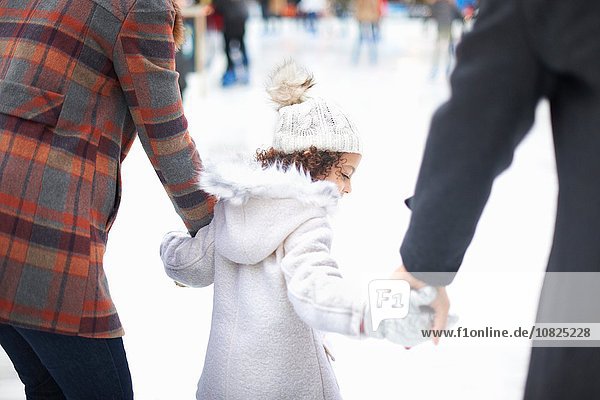 Rear view of girl ice skating with parents  holding hands
