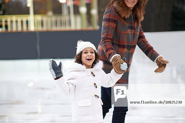 Girl ice skating with mother  holding hands looking at camera smiling
