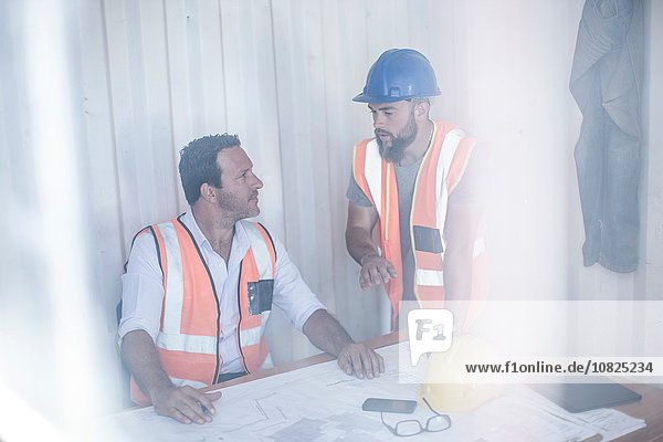 Construction foreman and builder meeting at desk in portable cabin