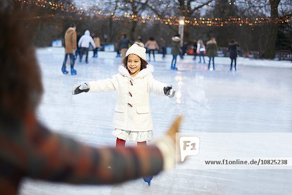 Girl on ice rink  arms open skating to mother smiling