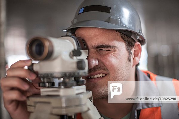 Young male surveyor looking through theodolite on construction site