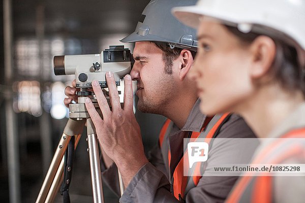 Female and male surveyors looking through theodolite on construction site