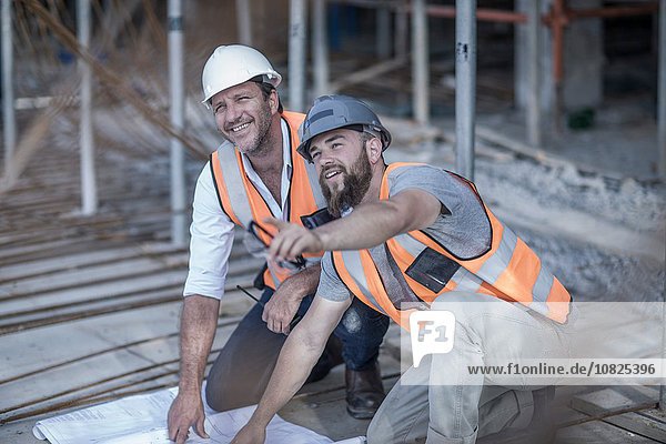Site manager and builder with blueprint on construction site