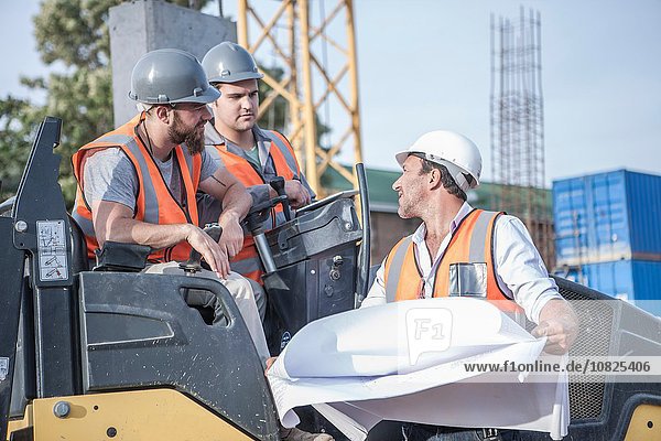 Bauleiter im Gespräch mit Dampfwalzenfahrern über den Bauplan auf der Baustelle
