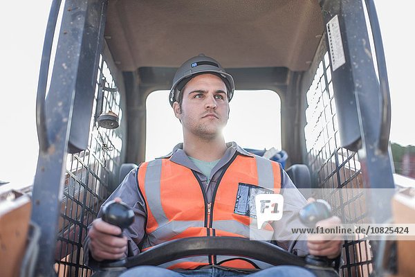 Young man driving excavator on construction site