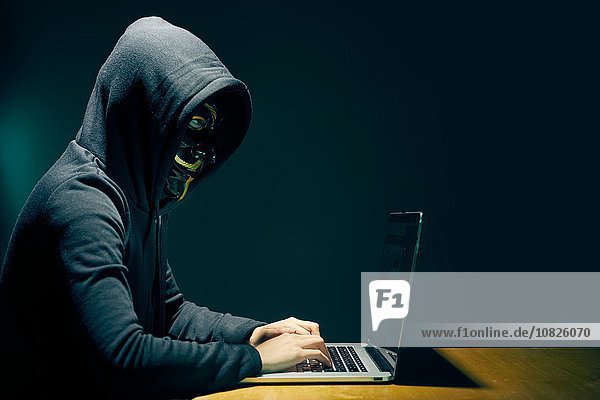 Seitenansicht der Person mit Kapuze und Guy Fawkes Gesichtsmaske mit Laptop
