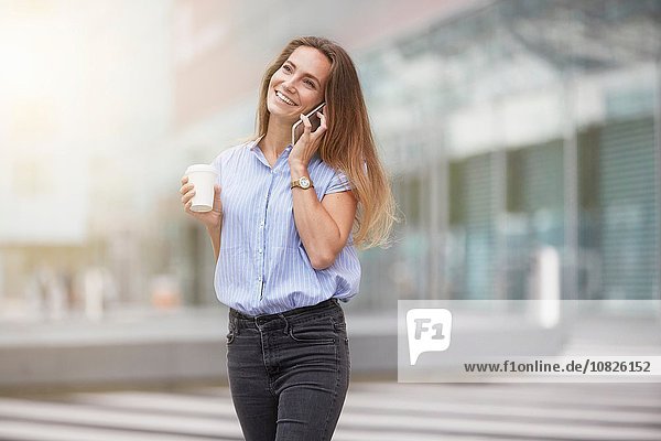Junge Frau telefoniert mit dem Smartphone und schaut lächelnd weg.