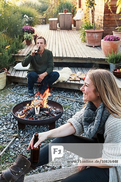 Mann und Frau sitzen an der Feuerstelle mit Bier und entspannen sich.