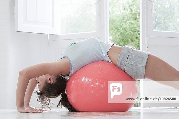 Junge Frau auf dem Rücken liegend auf rosa Übungsball zu Hause