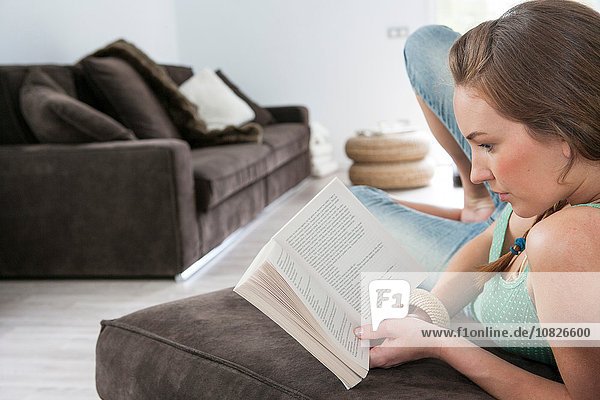 Junge Frau liegt auf dem Sofa und liest ein Buch.