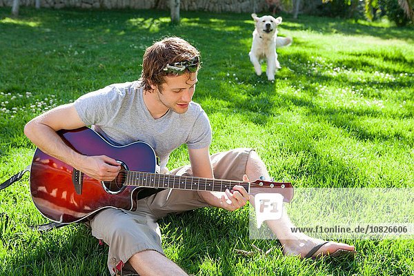 Junger Mann sitzt im Garten und spielt Akustikgitarre.
