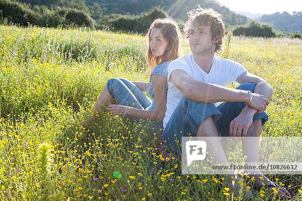 Romantic young couple sitting back to back in wildflower field  Majorca  Spain