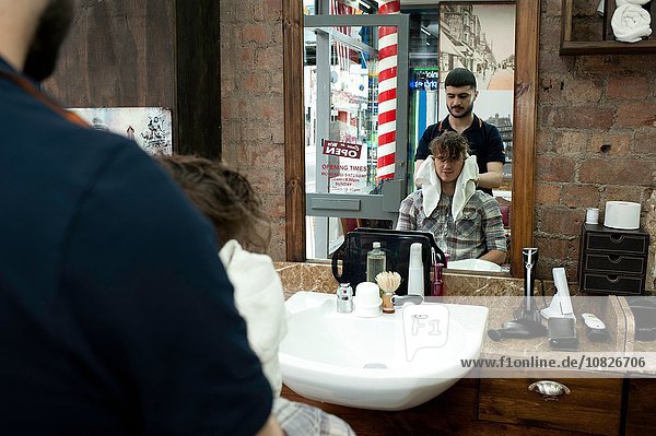 Spiegelbild des jungen Mannes und Friseurs im Friseursalon