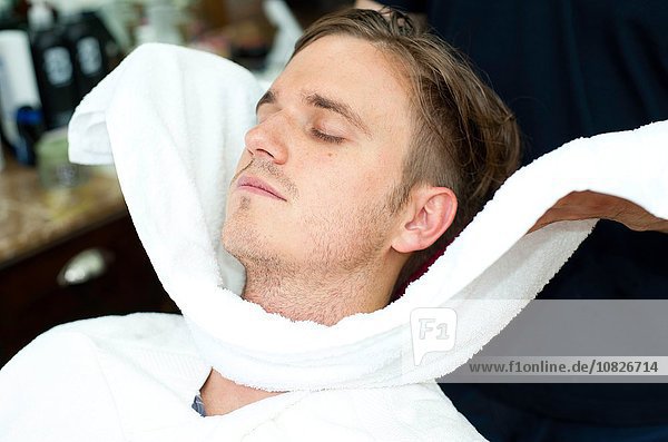 Junger Mann  Auge geschlossen  Gesicht in frisches Handtuch gehüllt