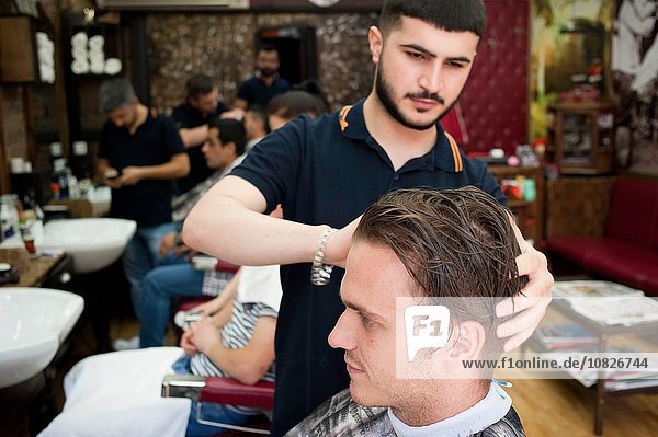 Hairdresser in barbershop cutting young mans hair