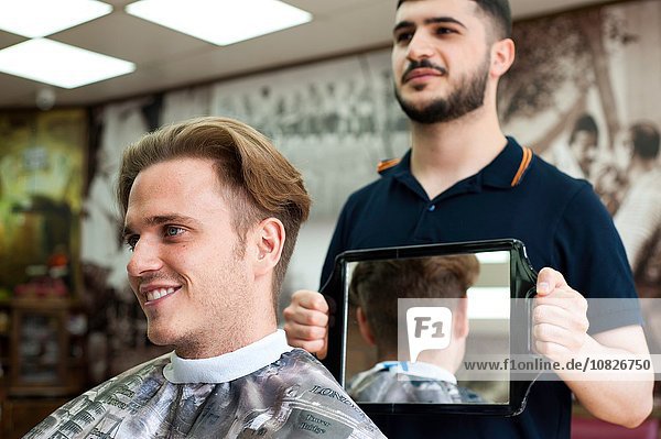 Friseur mit Spiegel für lächelnden Kundenhaarschnitt