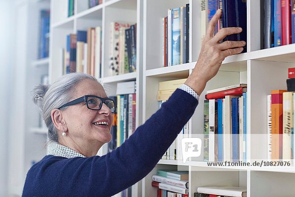 Glückliche  grauhaarige  reife Frau  die ein Buch aus dem Bücherregal auswählt.