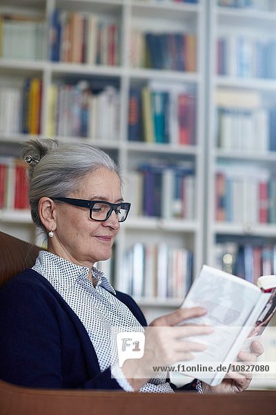 Grauhaarige reife Frau liest Buch aus dem Bücherregal