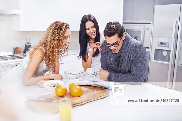 Drei junge Erwachsene lesen Zeitung am Küchentisch