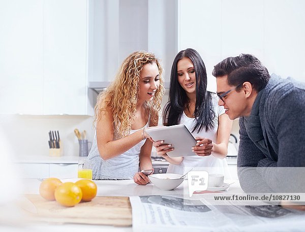 Drei junge Erwachsene mit digitalem Tablett an der Küchenzeile
