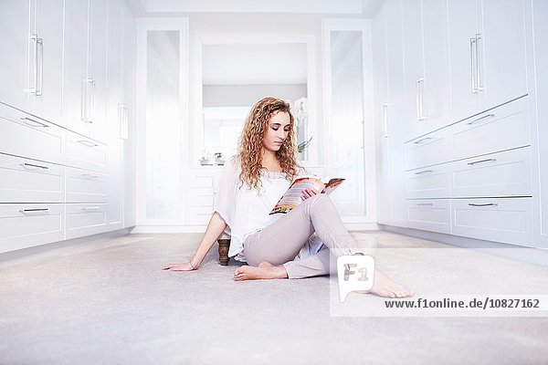 Young woman sitting on floor reading a book in bedroom