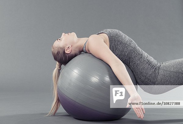 Junge Frau beim Yoga mit Gymnastikball,  grauer Hintergrund