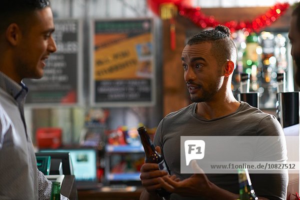 Young man in public house holding beer bottle talking to friend