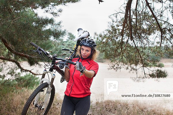 Portrait of woman mountain biker carrying cycle over sand on riverbank