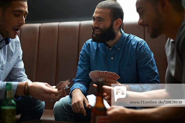 Three young adult male friends playing card game in traditional UK pub