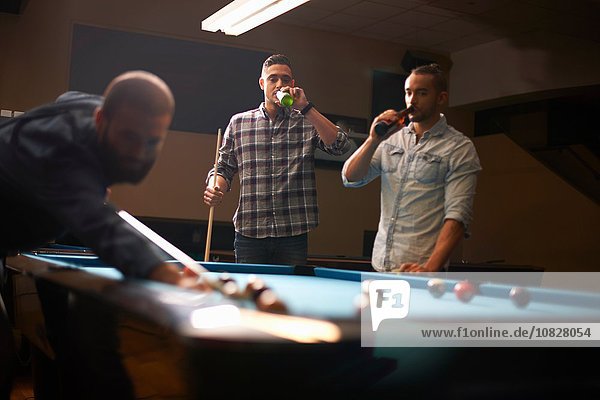 Man playing pool  friends drinking beer in background