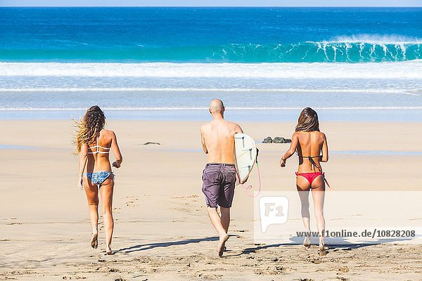 Rückansicht des männlichen Surfers und zweier junger Frauen in Badebekleidung am Strand El Cotillo Fuerteventura Spanien