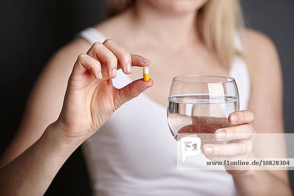 Schnappschuss einer jungen Frau mit Medikamentenkapsel und Wasserglas