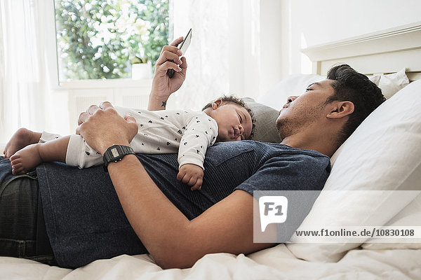 Vater benutzt Mobiltelefon mit schlafendem Babysohn