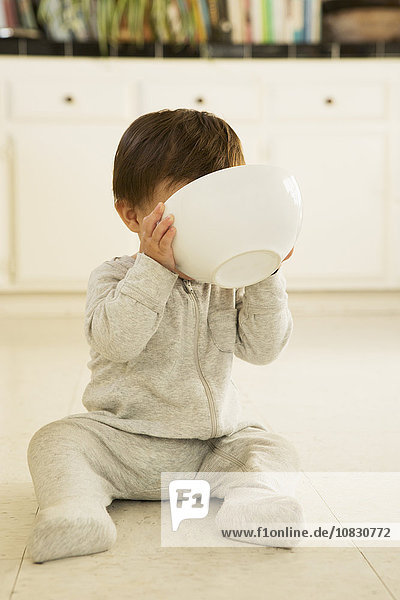 Mixed race baby boy drinking from bowl on floor