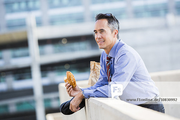 Gemischtrassiger Geschäftsmann isst auf dem Dach einer Stadt