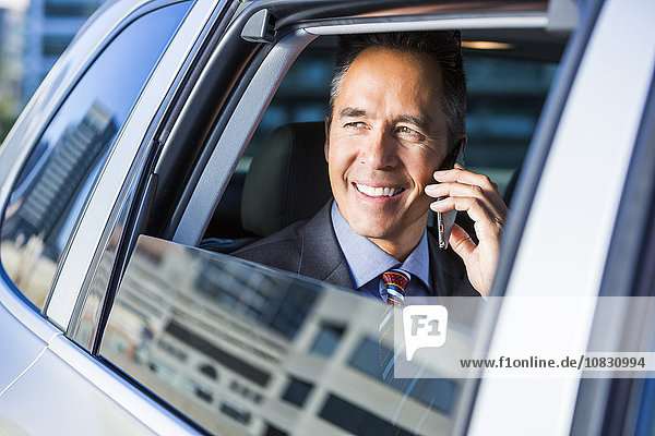 Mixed race businessman talking on cell phone in car