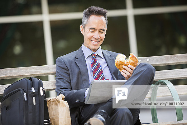 Mixed race businessman eating and using digital tablet