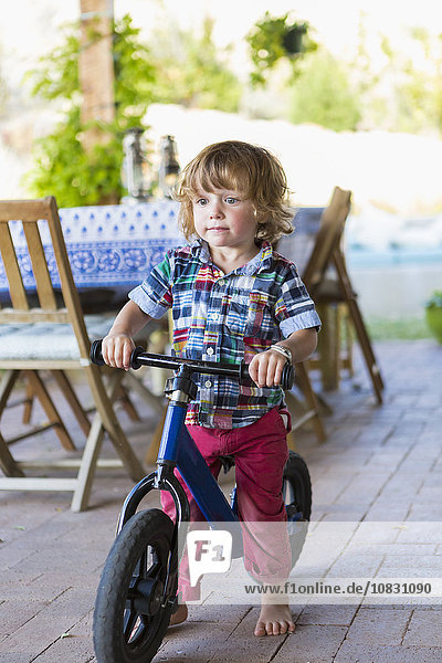 Caucasian boy riding bicycle on patio