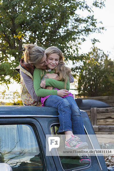 Caucasian mother hugging daughter on roof of truck