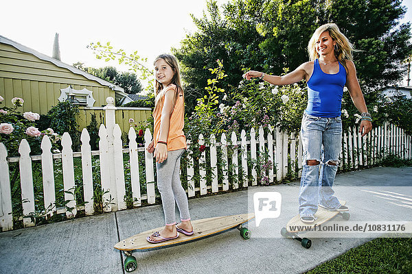 Kaukasische Mutter und Tochter fahren Skateboard auf dem Bürgersteig