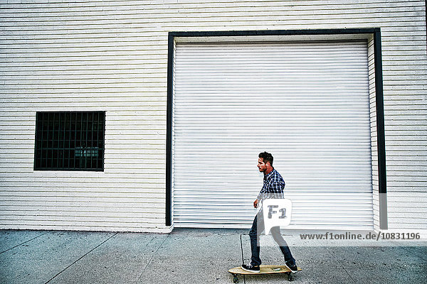 Caucasian man riding skateboard on sidewalk