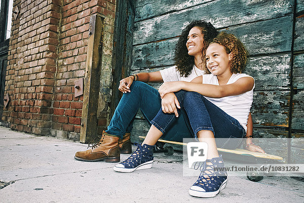 Mixed race mother and daughter sitting on skateboard