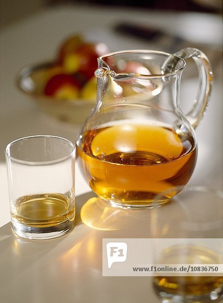 Apfelsaft in Glaskrug und Gläsern im Sonnenlicht vor einer Schale mit frischen Äpfeln