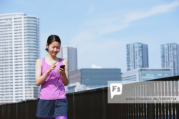 Junge Japanerin mit Smartphone vor ihrem Lauf in der Innenstadt von Tokio