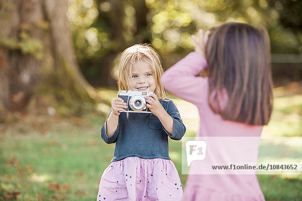 Toddler girls playing with camera in park