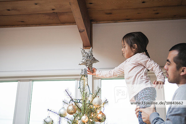 Vater hebt Kleinkind Mädchen setzt Stern auf Weihnachtsbaum