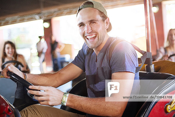 Lachender junger Mann auf Autoscooter im Vergnügungspark