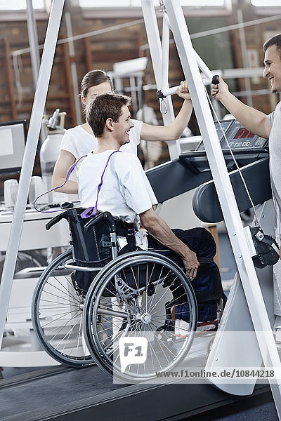 Physiotherapeuten führen Mann im Rollstuhl auf dem Laufband