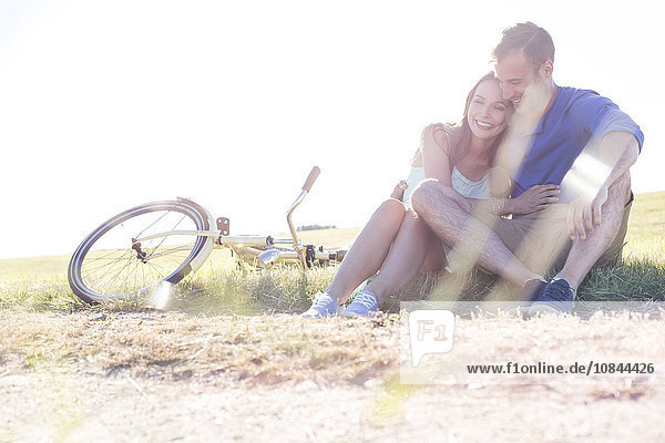 Zärtliches junges Paar  das sich in der Nähe des Fahrrads in ländlichem Gras umarmt