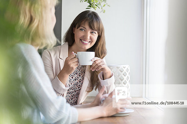 Lächelnde Frauen beim Kaffeetrinken am Caféfenster